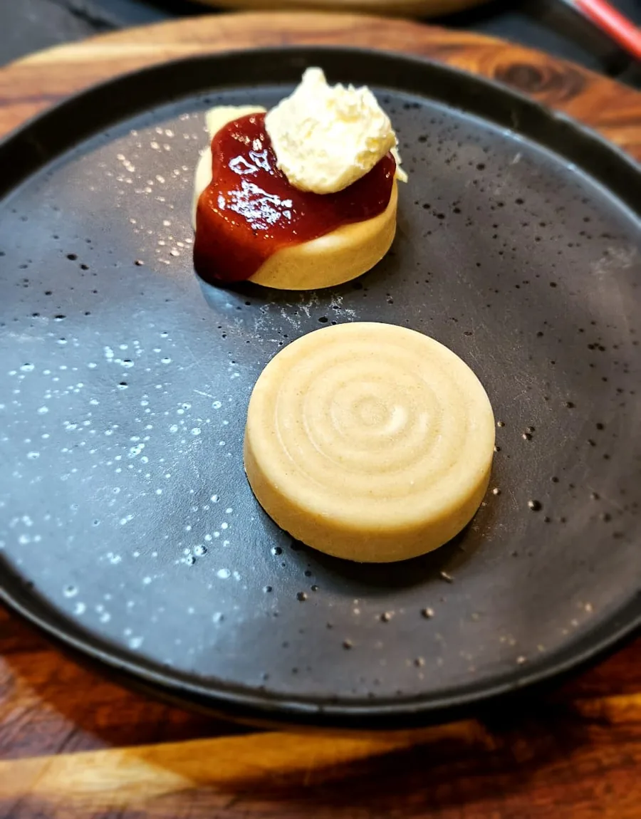 An Ocras scone with jam and cream beside a plain moulded scone